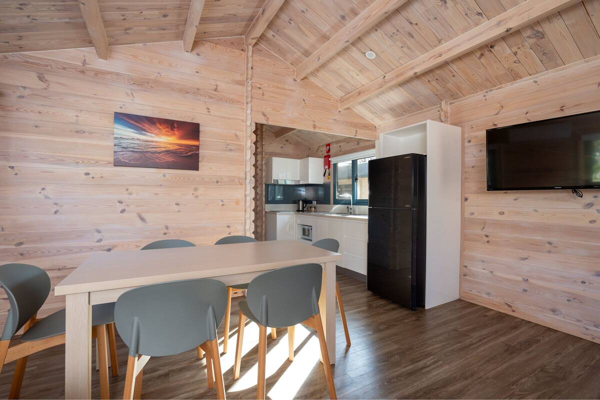 A modern kitchen with white cabinets, a black refrigerator, and a flat-screen TV mounted on the wall.