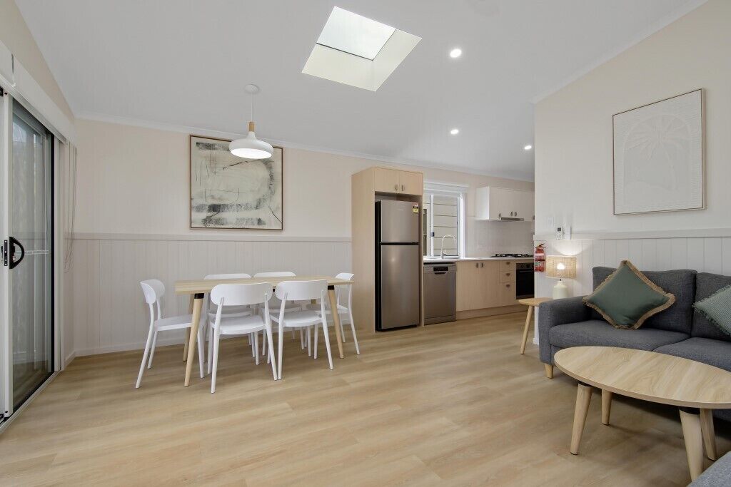 Una cocina moderna con refrigerador, estufa y comedor con sillas y mesa.