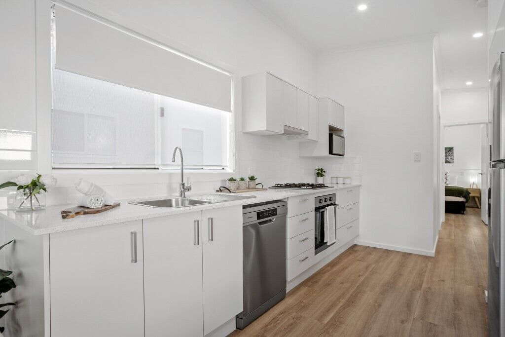 Una cocina moderna con armarios blancos, lavavajillas, horno y ventana que deja entrar luz natural.