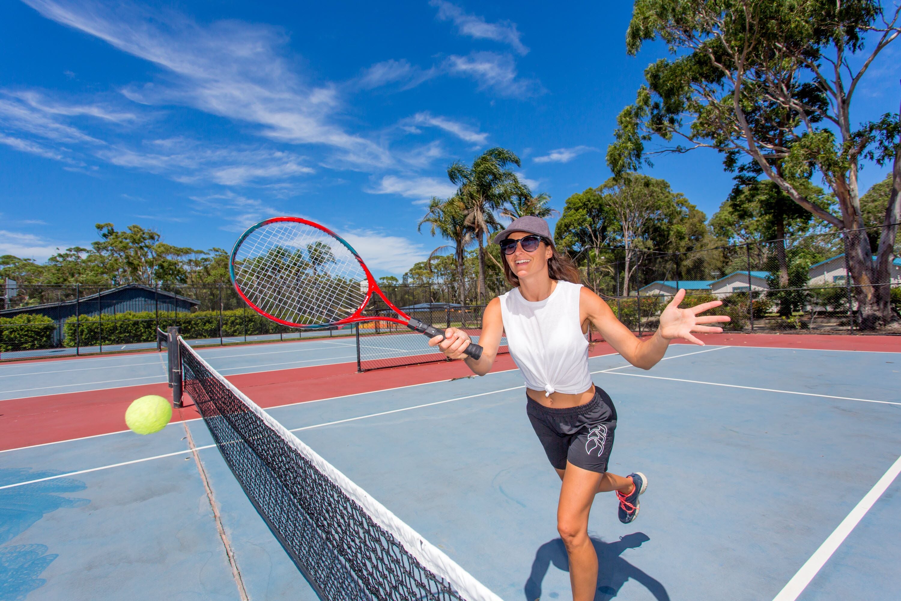 Een tennisbaan met een net, een tennisbal en een spelende tennisser.