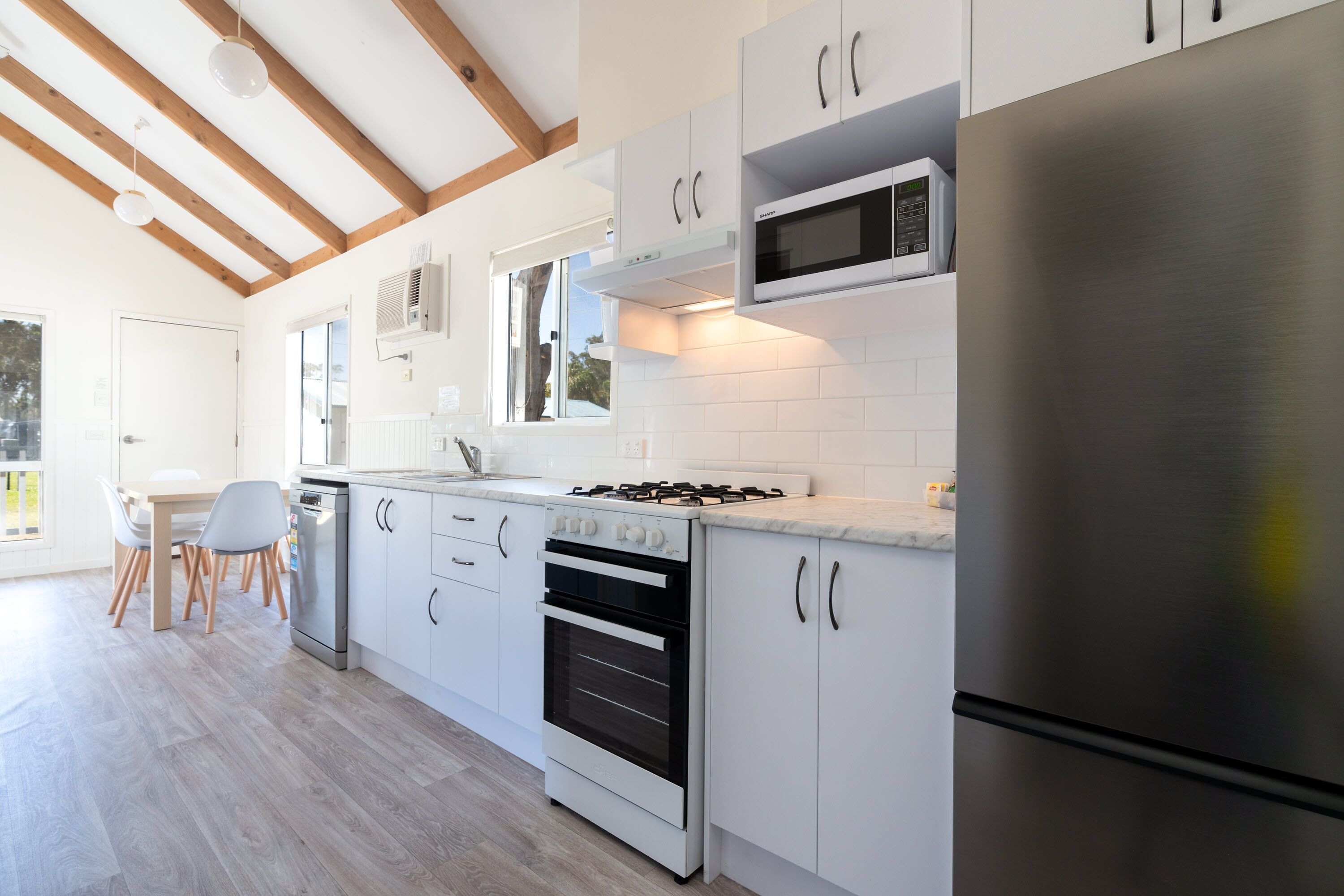 A modern kitchen with white cabinets, a stainless steel refrigerator, a built-in microwave, and a gas stove.