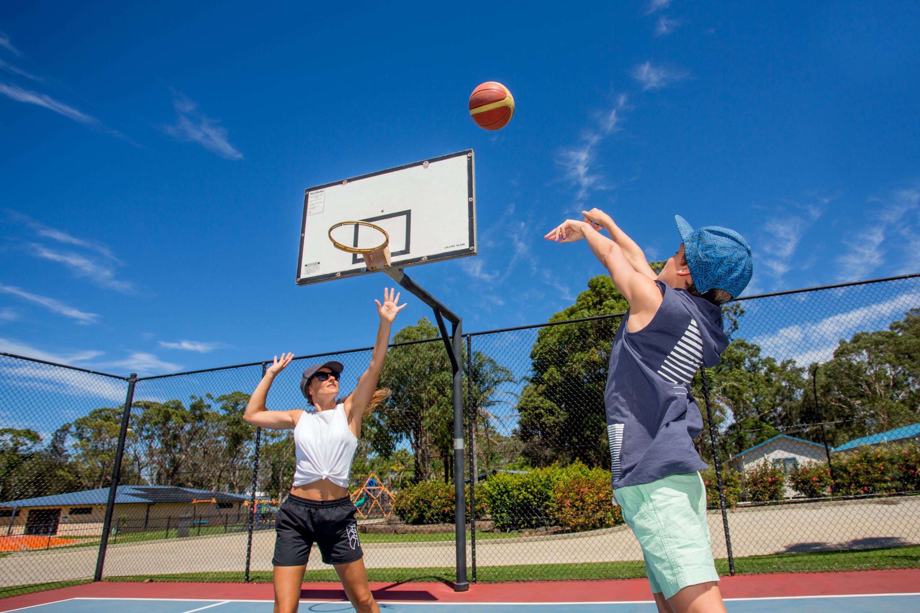 Ein Basketballplatz mit Netz umzäunt, einem Basketballkorb und blauem Himmel.