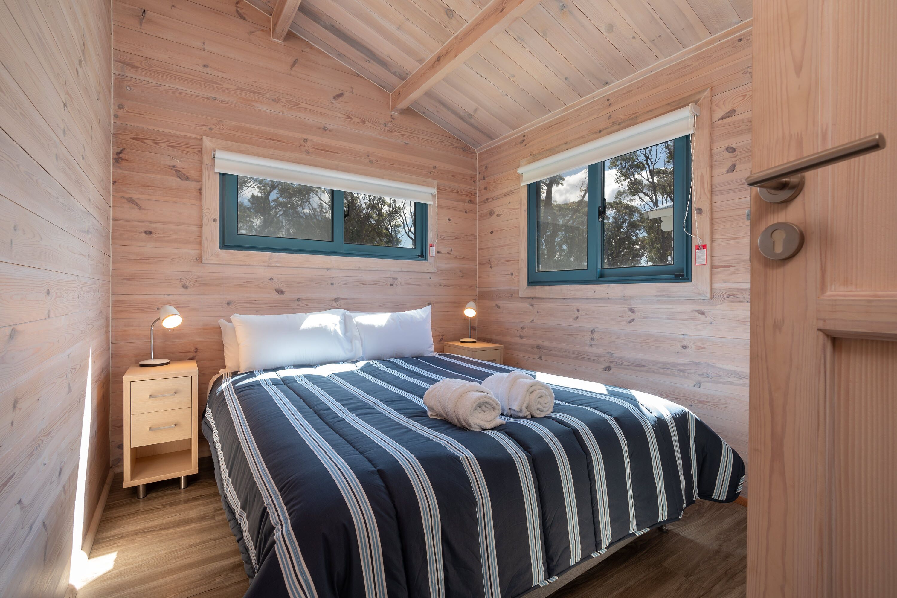 Un dormitorio con paneles de madera, una cama, dos mesitas de noche y dos ventanas.