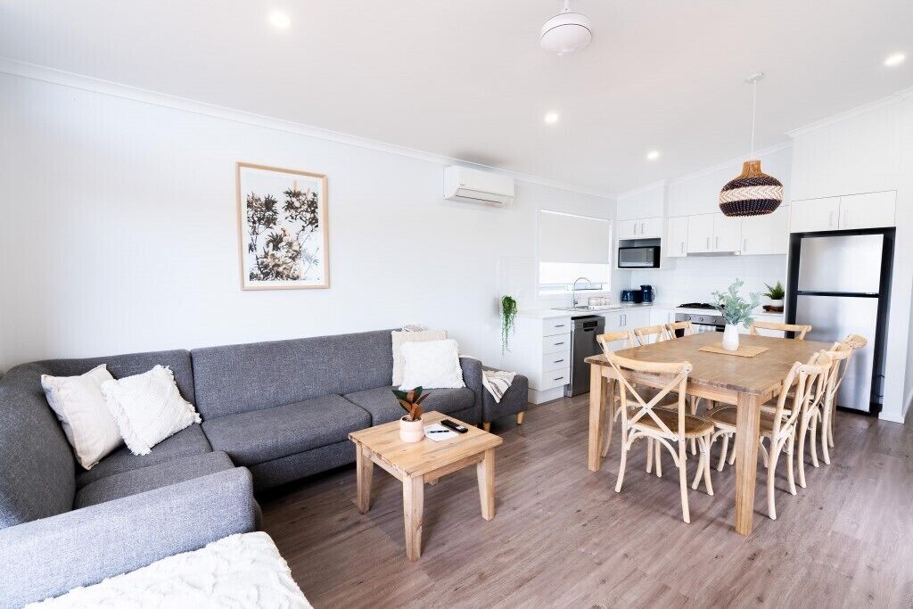 A modern living room with a grey sofa, wooden coffee table, and dining table with chairs.