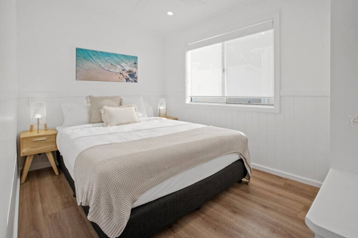 A bedroom with a bed, bedside tables, a window, and a wall-mounted picture.