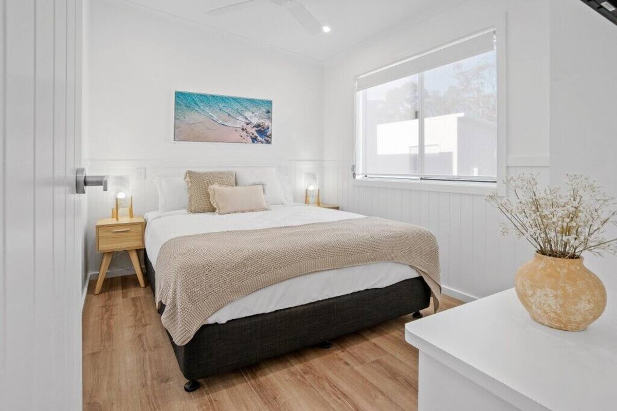 A bedroom with a bed, bedside tables, a window with a view, and a painting on the wall.