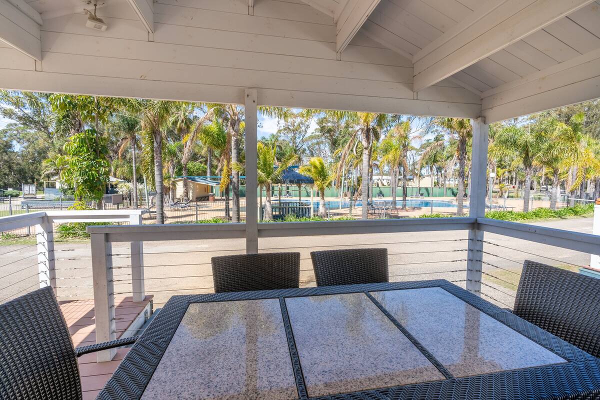 A covered outdoor seating area with a table and chairs, overlooking a pool and palm trees.