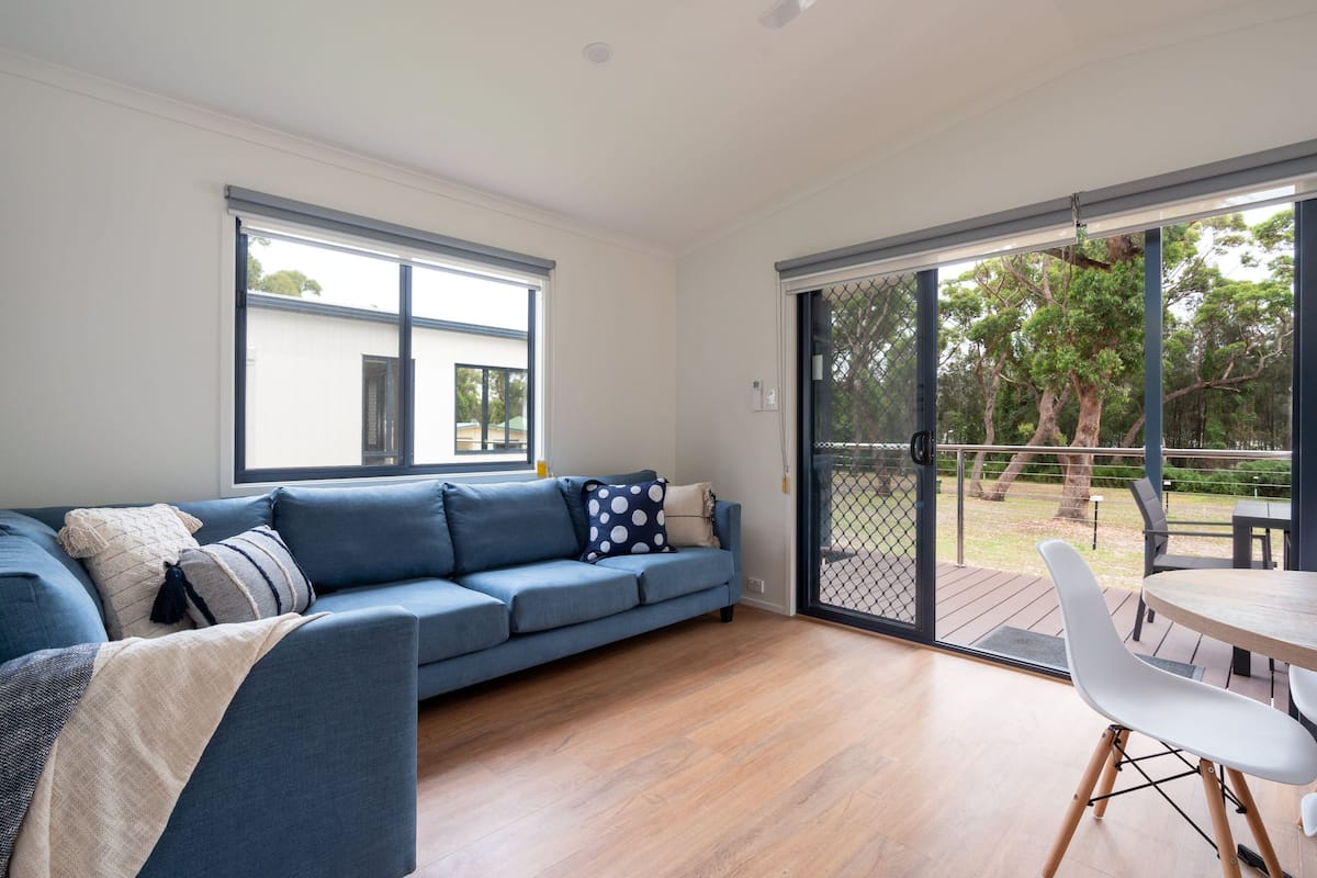 A modern living room with a blue sofa, a dining table, and a sliding glass door leading to an outdoor area.