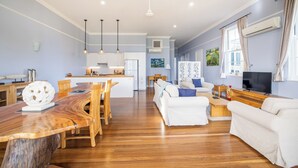 Un vaste espace de vie comprenant une table à manger en bois, des canapés blancs et une cuisine à l’arrière-plan.