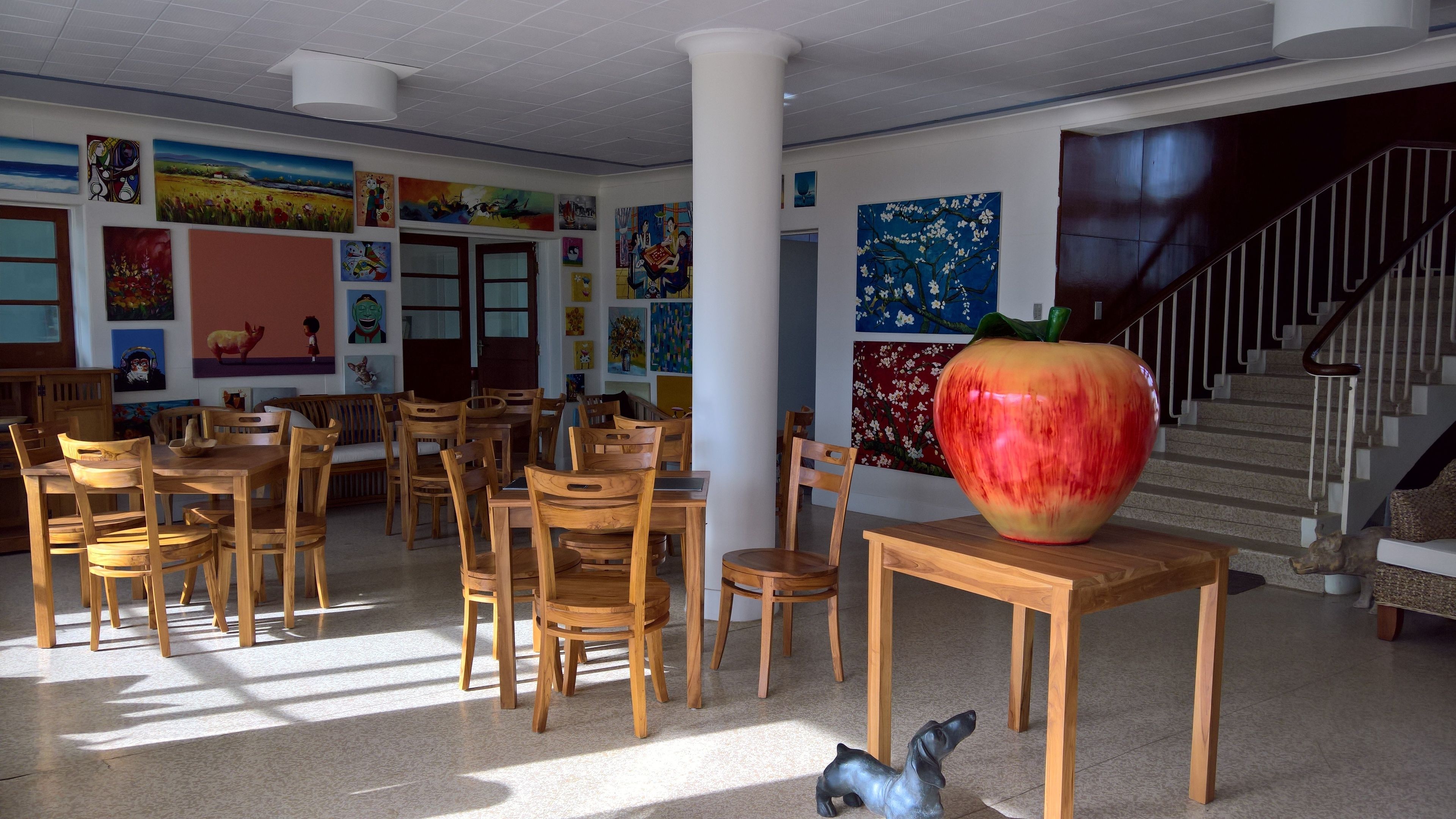 A dining area with wooden tables and chairs, a large apple sculpture, and colorful artwork on the walls.