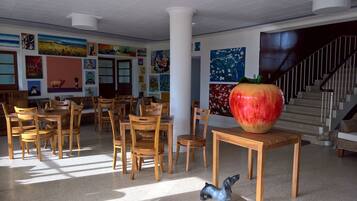 A dining area with wooden tables and chairs, a large apple sculpture, and colorful artwork on the walls.