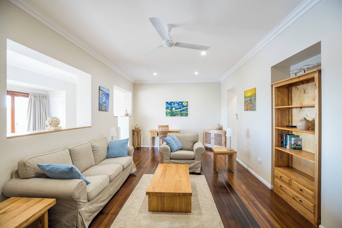 Una sala de estar con sofá, sillón, mesa de centro y estantería de madera.