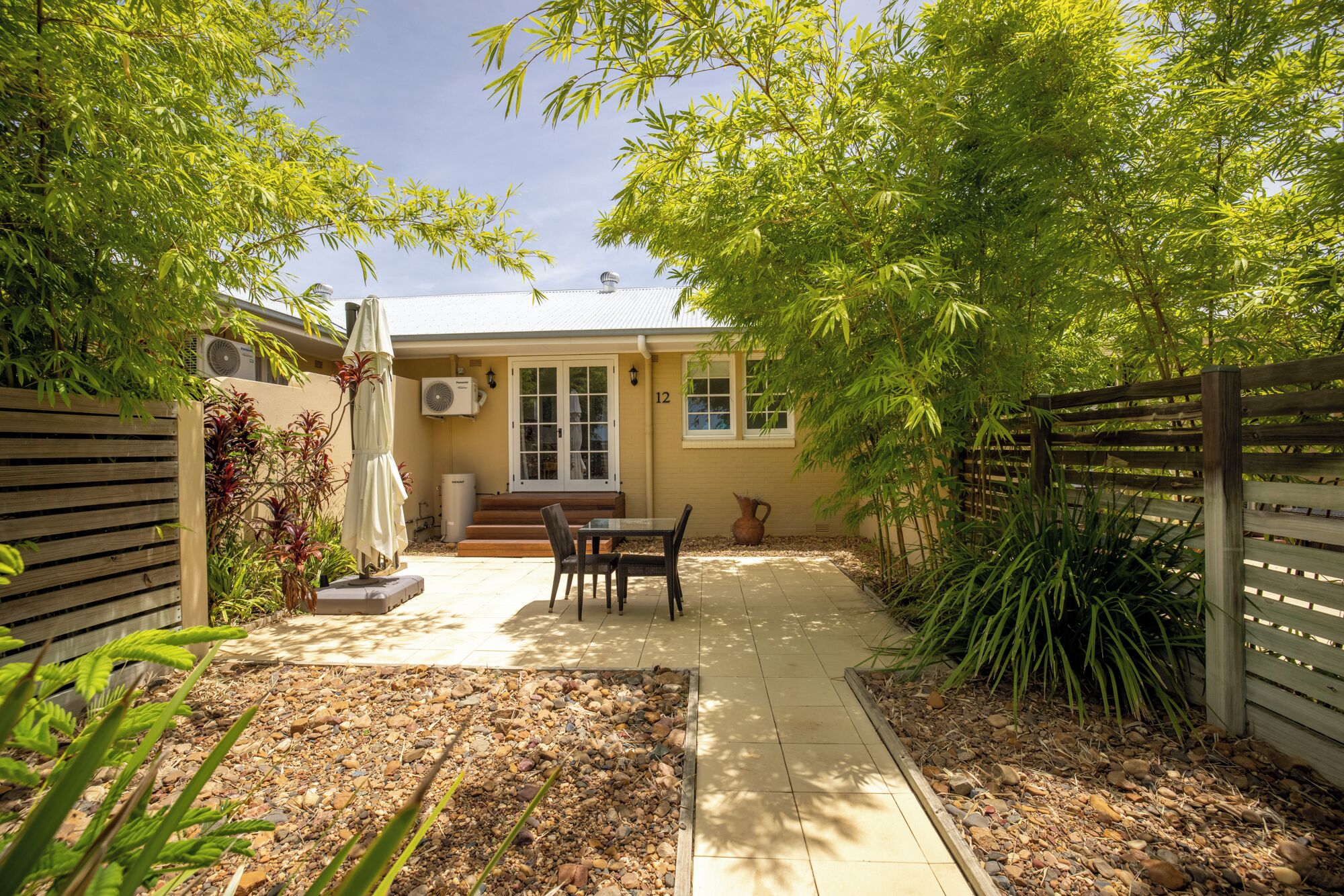 A patio area with a table and chairs, surrounded by a wooden fence and greenery.