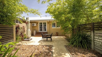 A patio area with a table and chairs, surrounded by a wooden fence and greenery.
