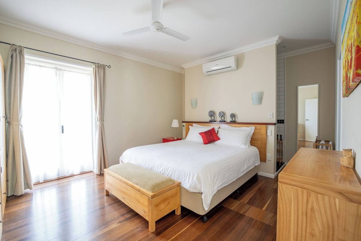 Habitación de hotel con cama, banqueta, escritorio, equipo de aire acondicionado y ventilador de techo.