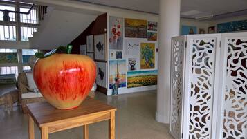 A large, colorful apple sculpture on a wooden table in a gallery with various artworks on the walls.