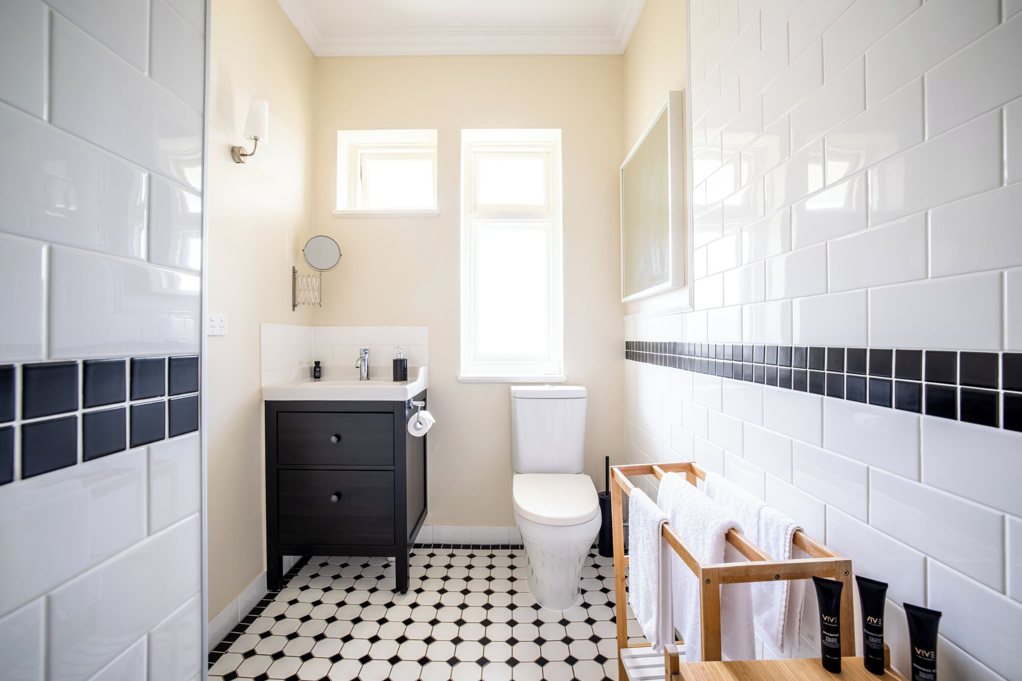 Un baño pequeño con suelo de baldosas blanco y negro, un lavabo blanco con espejo y un inodoro.