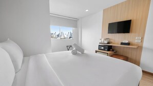 Una habitación de hotel moderna con una cama grande, un televisor montado, vistas a la ciudad y una pequeña zona de estar.
