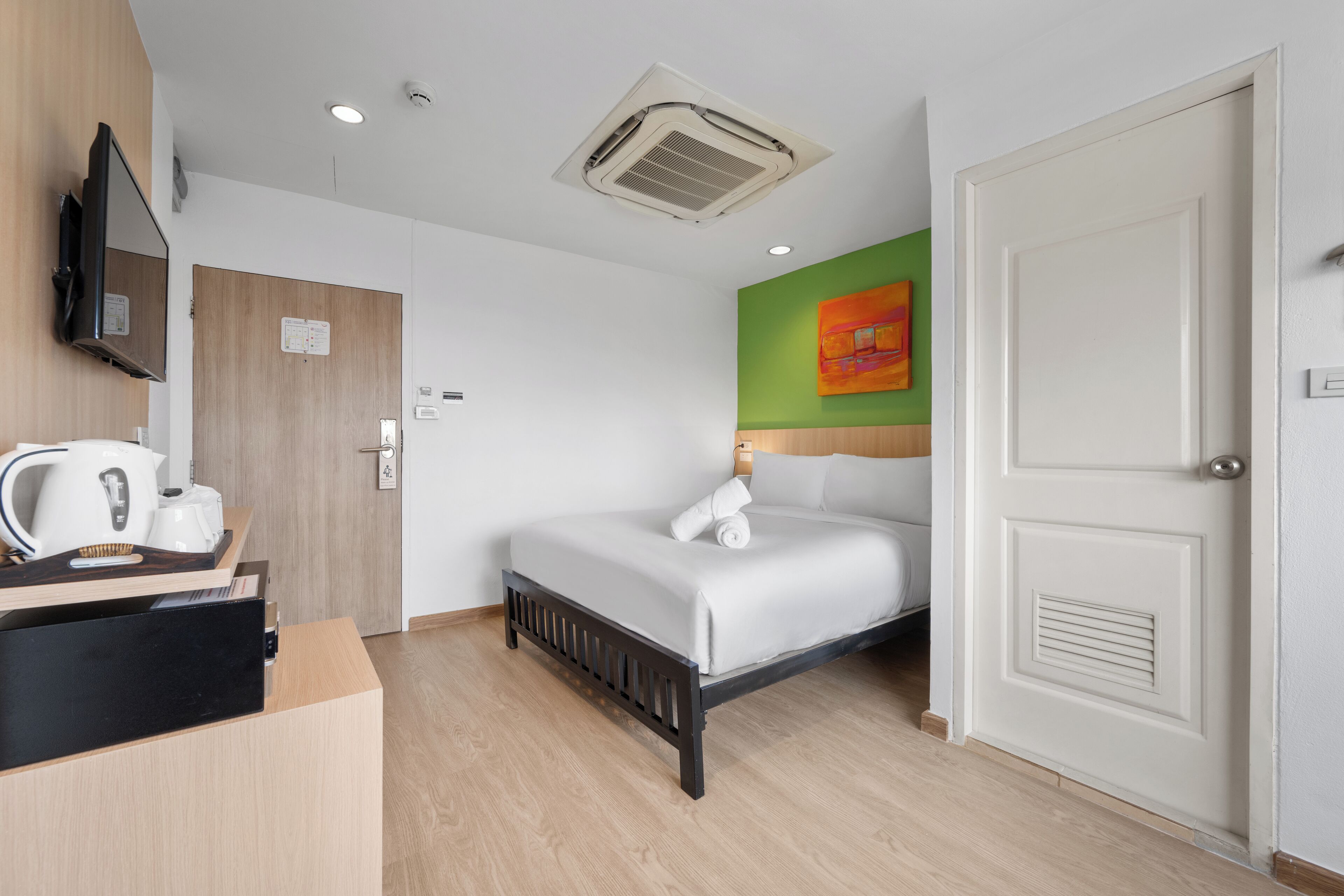 A hotel room with a bed, a desk with a kettle, a television, and a green accent wall.