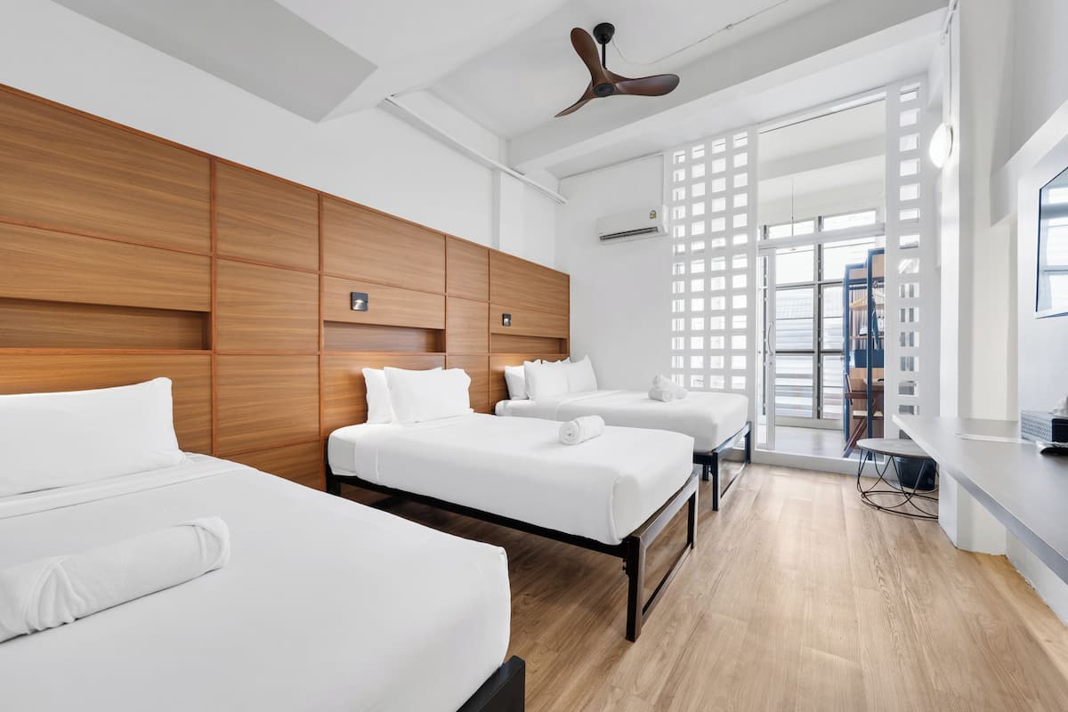 Ein Hotelzimmer mit drei Betten, Holz-Kopfteilen, einem Deckenventilator und Blick durch eine Glastür.