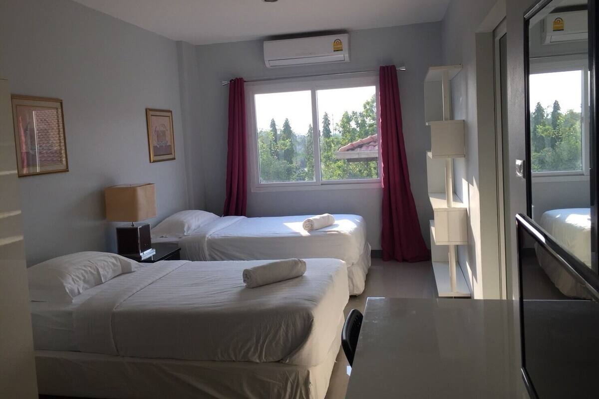 A hotel room with two beds, a desk, a chair, and a window with curtains.