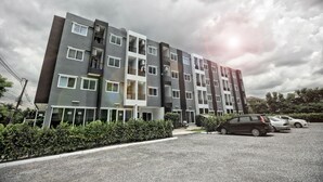 A multi-story residential building with balconies, a parking area, and a gravel driveway. - I-Beyond Residence (Bangkok)