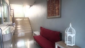 A hallway with a red sofa, a white birdcage, and a staircase leading to another room. - I-Beyond Residence (Bangkok)