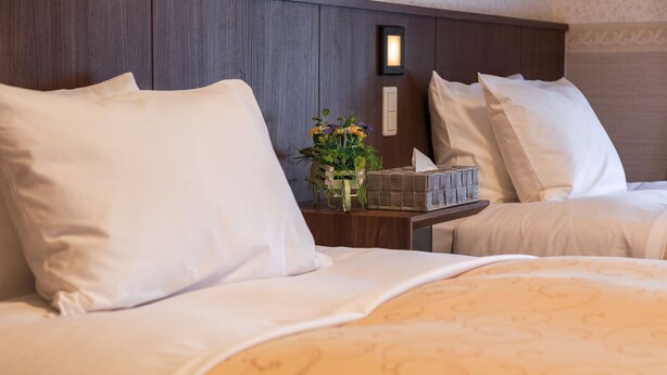 A hotel room with a large bed, a nightstand with a vase of flowers, and a wall-mounted light. - Hotel Quartz Shin Osaka (Osaka)