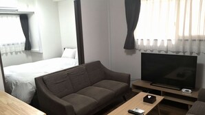 A hotel room with a sofa, a TV, a wooden coffee table, and a bed with curtains. - Hotel Quartz Shin Osaka (Osaka)