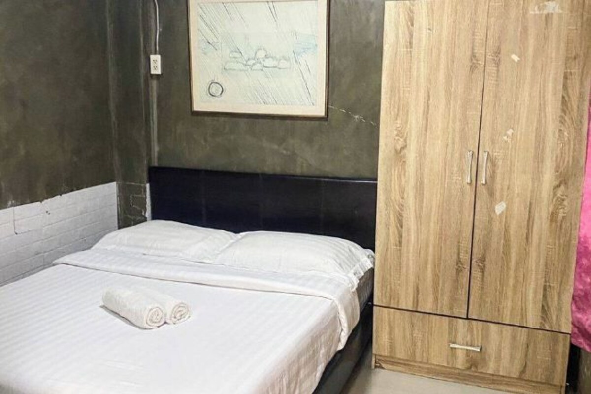 A bedroom with a bed, a wooden wardrobe, and a framed picture on the wall.