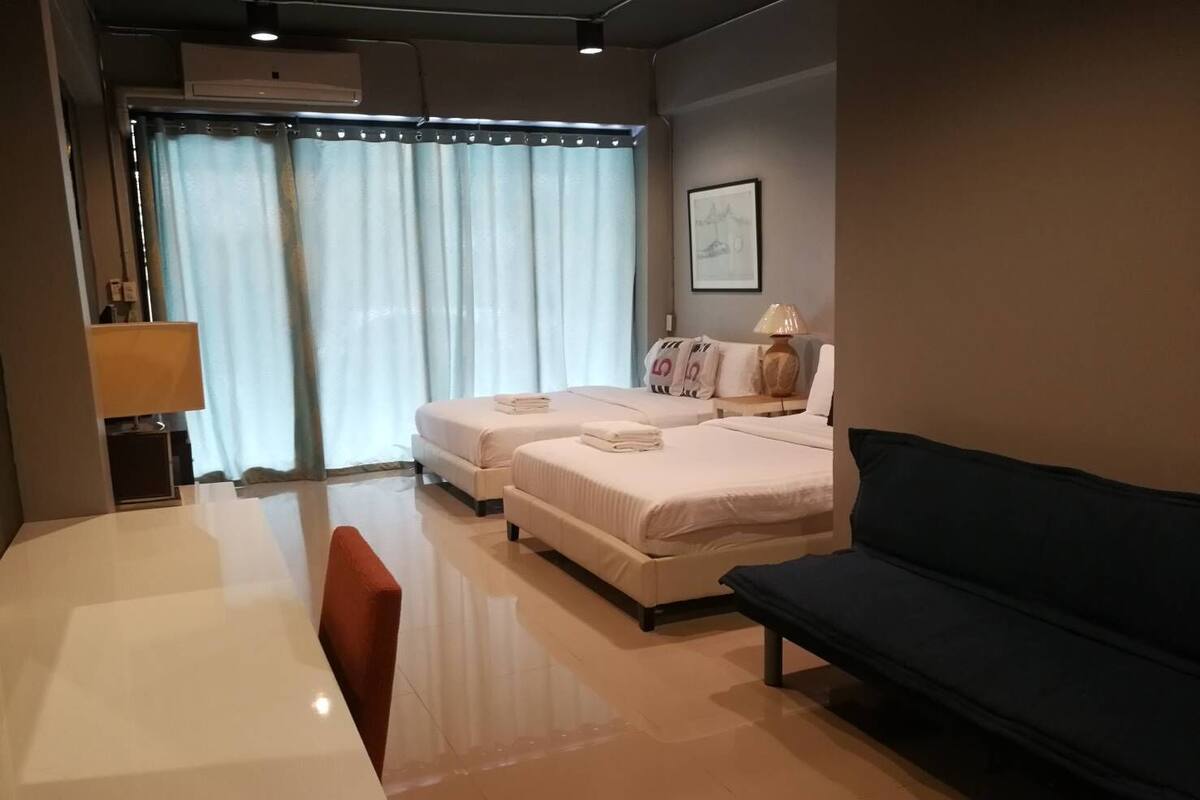 Une chambre d’hôtel avec deux lits, un bureau, une chaise, un canapé et une fenêtre avec des rideaux.