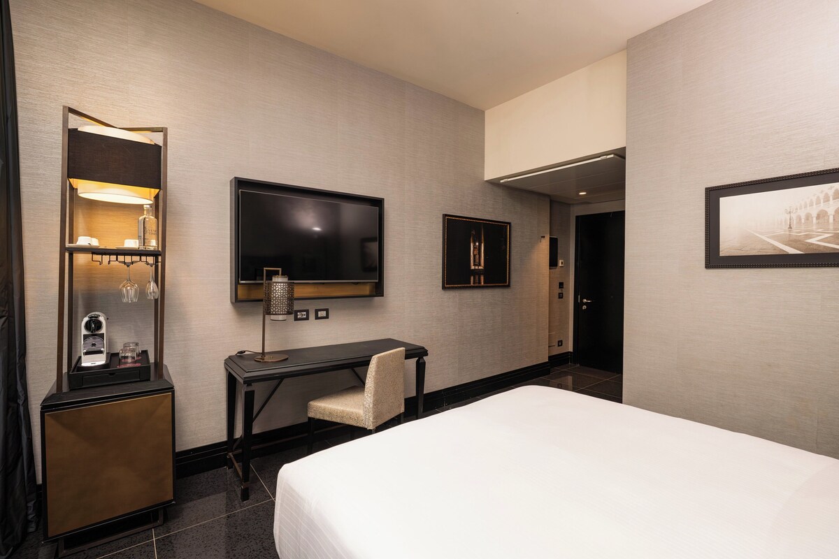 Una habitación de hotel con cama, escritorio, televisión, minibar y puerta.