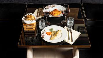 A dining table with a plate of food, two wine glasses, and a basket of bread.