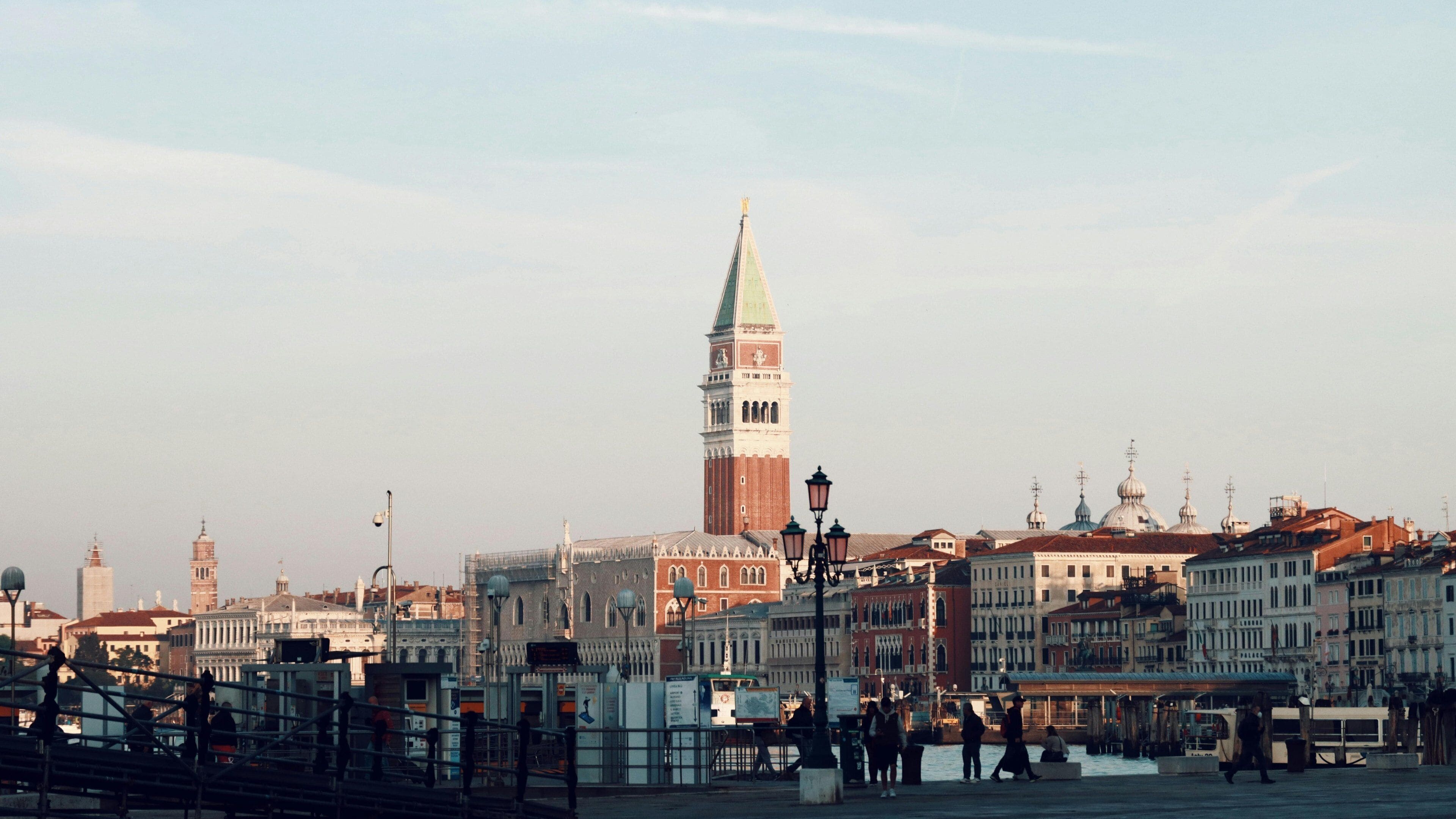 A historic cityscape with prominent architecture, including a tall tower with a clock, and a waterfront area with buildings and a bridge.
