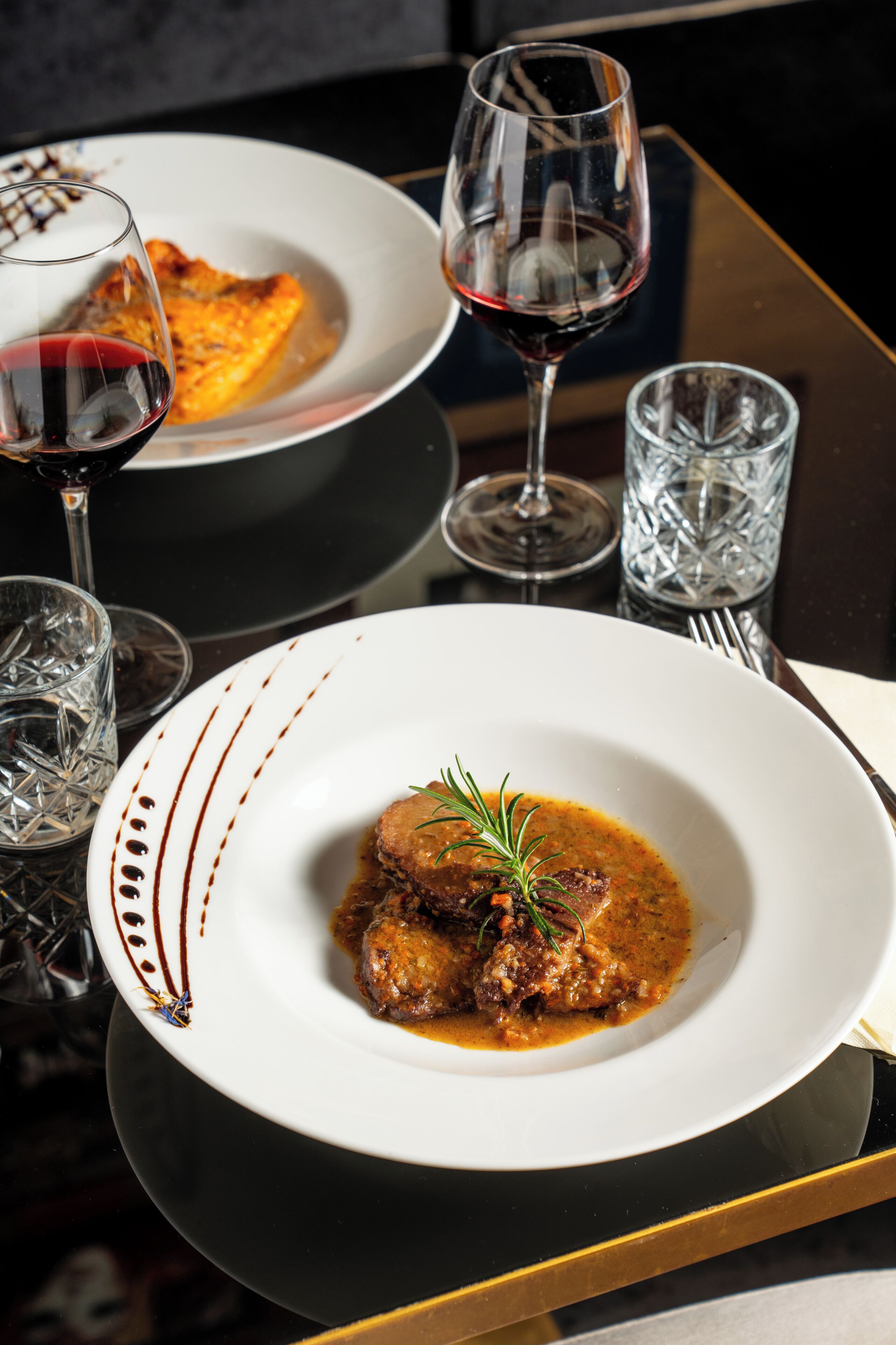 Une table à manger avec une assiette de nourriture, un verre de vin rouge et un verre d’eau.
