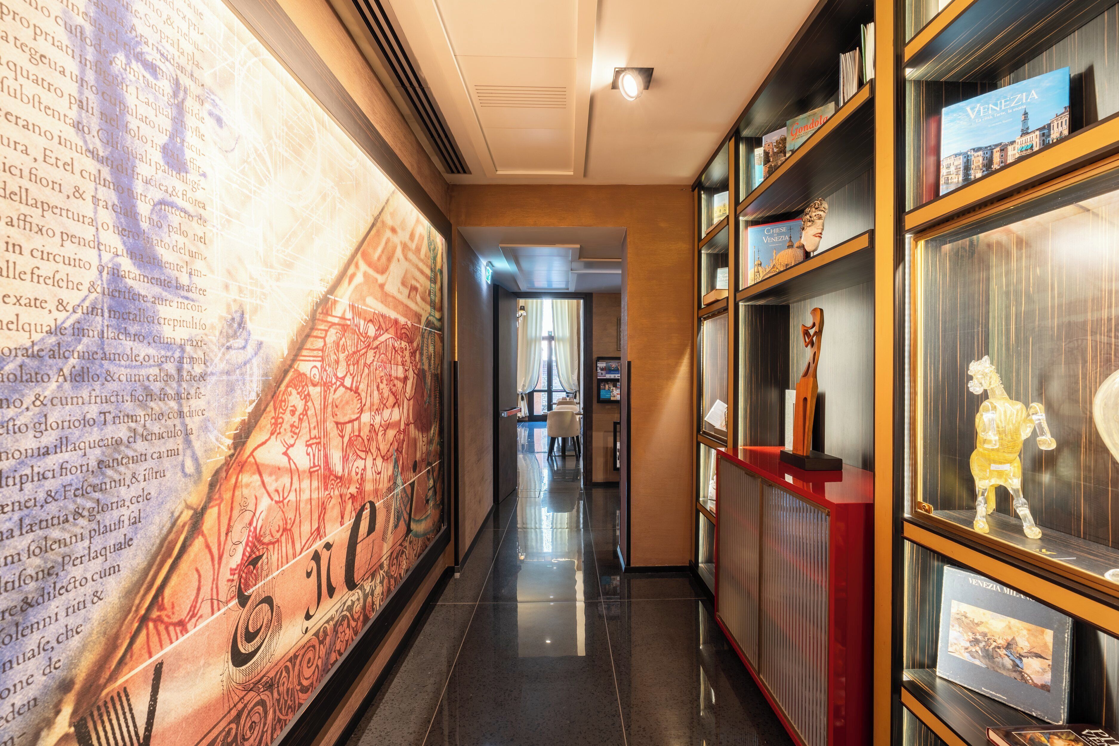 A hallway with a large mural, bookshelves with books and decorative items, and a red reception desk.