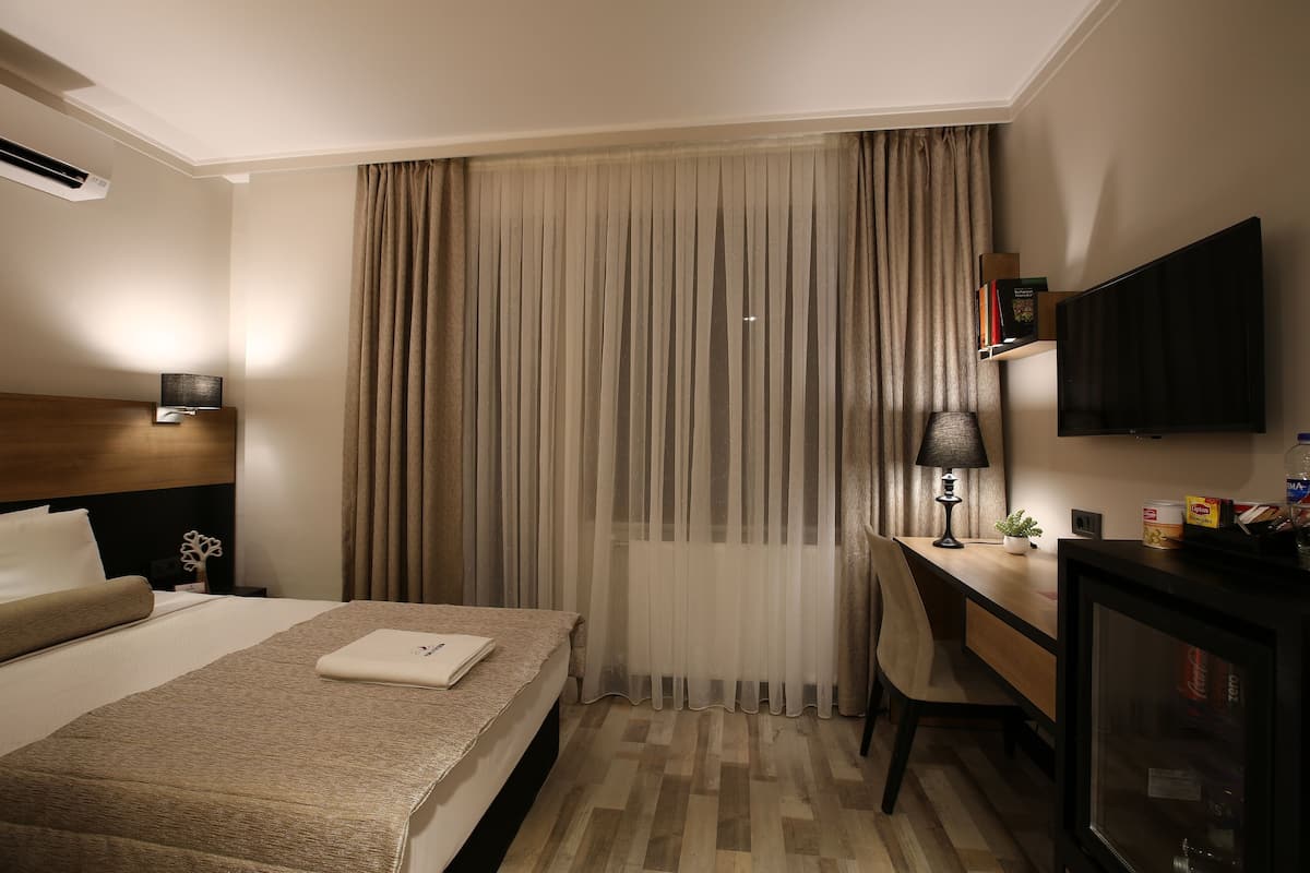 A hotel room with a bed, a desk, a chair, a television, and a bookshelf.