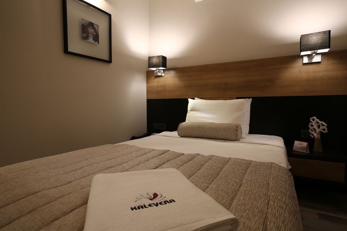 A hotel room with a neatly made bed, two wall-mounted lamps, a framed picture on the wall, and a nightstand with a decorative item.