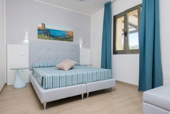 A bedroom with a bed, a painting, a window with curtains, and a bedside table. - Eden Resort Country & Spa (Ugento)
