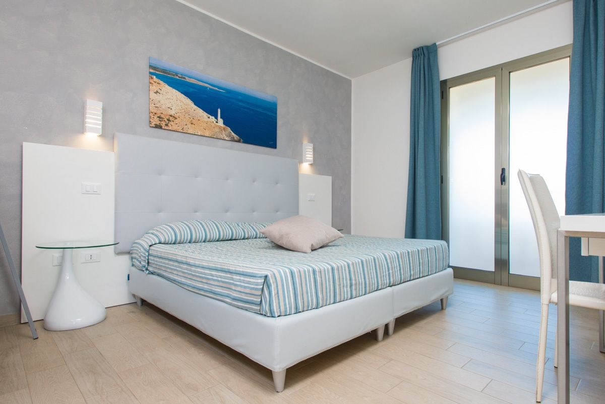 Un dormitorio con cama, una mesa de vidrio, una silla, un cuadro y una puerta corredera.