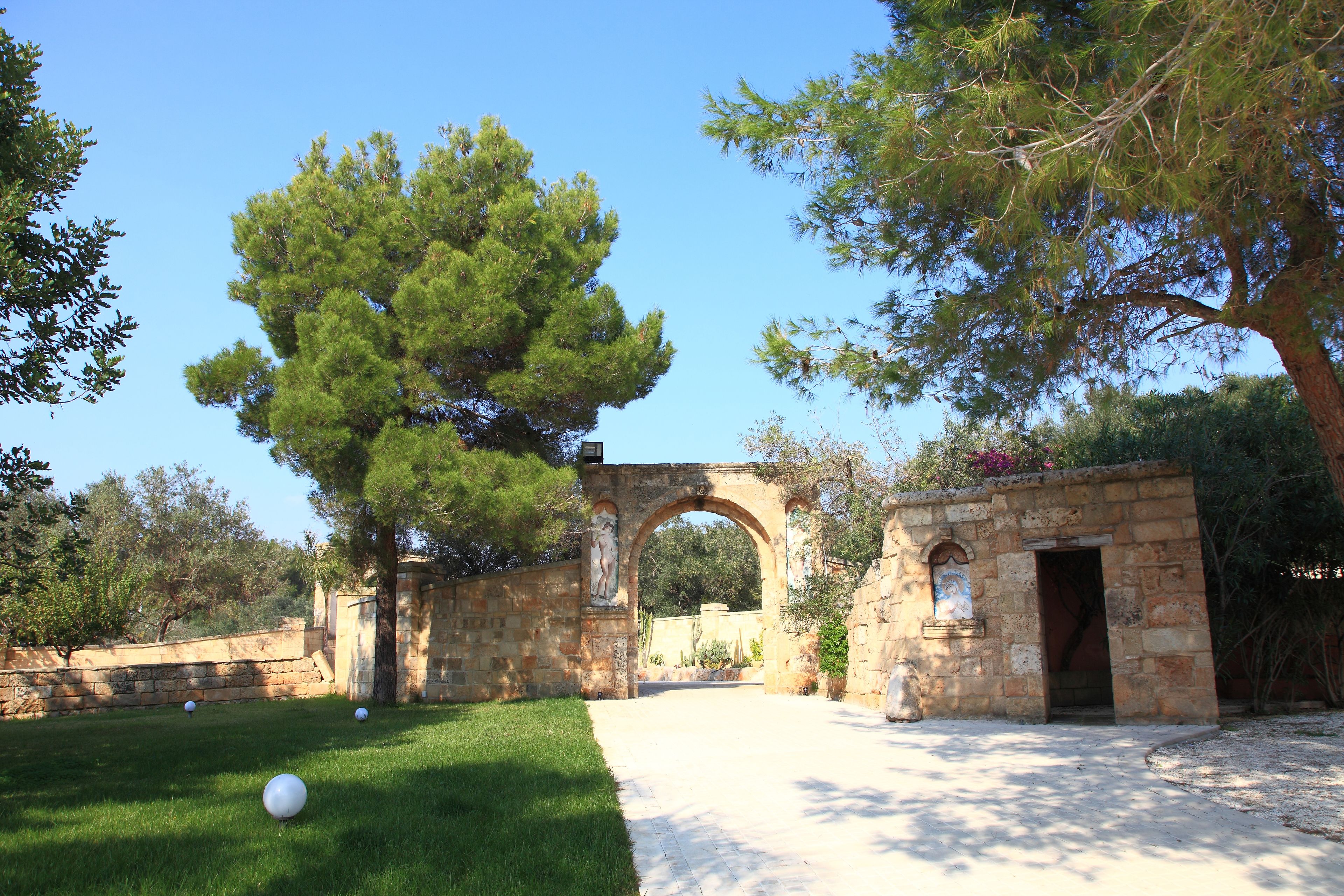 An outdoor area with a stone archway, a grassy lawn, and a pathway leading through the archway.