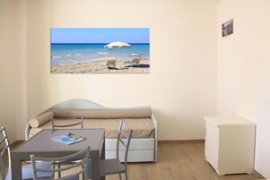 Una habitación con vista al mar, un sofá, una mesa con sillas y un mueble pequeño.
