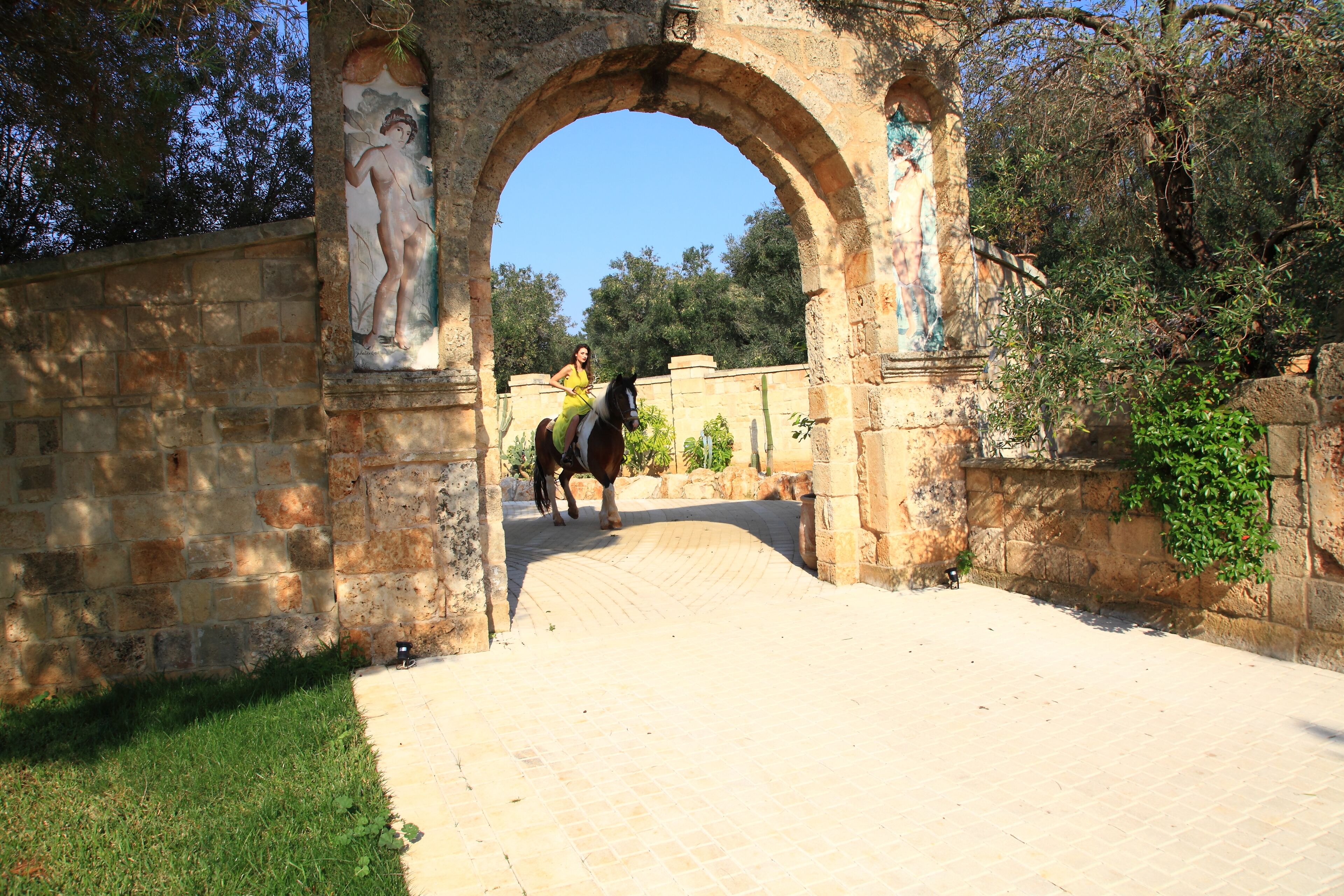 Un arco in pietra con un murale, che conduce a un viale lastricato.
