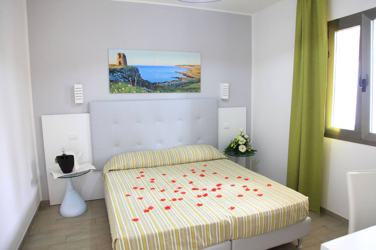 A bedroom with a bed, a painting on the wall, a bedside table, and a window with curtains.