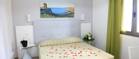 A bedroom with a bed, a painting on the wall, a bedside table, and a window with curtains.
