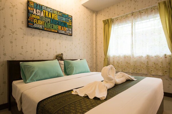 A hotel room with a bed, a wall with a word cloud, and a window with curtains.