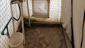 A small, dimly lit room with a single sink, a bucket, and a window with a curtain. - Golden Mark Camp (Leh)