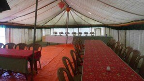 A tented dining area with tables and chairs, a buffet setup, and hanging lanterns. - Golden Mark Camp (Leh)