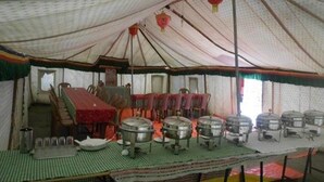 A large tent with a dining area, tables, chairs, and several large metal containers. - Golden Mark Camp (Leh)