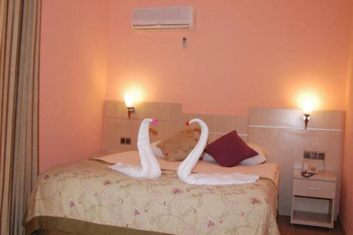 Habitación de hotel con cama, dos lámparas de pared, una mesita de noche y un equipo de aire acondicionado.